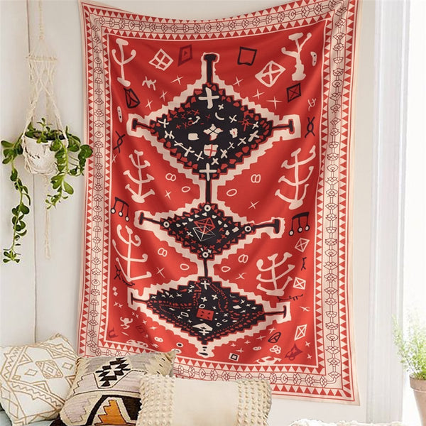 Red tapestry with black and white geometric tribal pattern hanging on a white wall above decorative pillows.