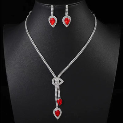 Silver-toned necklace and earring set with red teardrop stones and clear marquise-cut accents on a black display. - Image 8