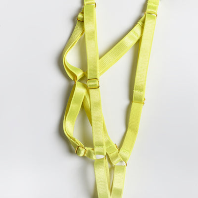 Woman in a neon yellow strappy harness lingerie set over a black lace bra and thong, sitting on a white bed. - Image 12