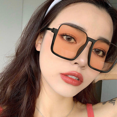 Retro square sunglasses with black frames and brown lenses held by a hand with patterned nails and a gold ring. - Image 3