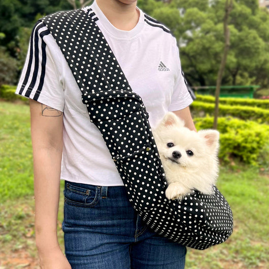 Person in white hoodie carrying a happy white dog in a navy blue pet sling bag outdoors. - Image 30