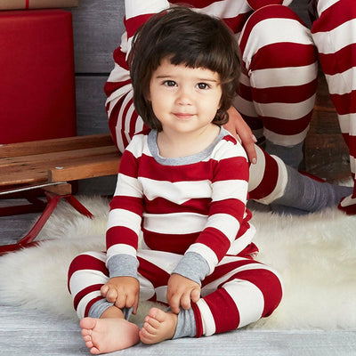 Family of four in matching red and white striped Christmas pajamas, sitting on a white rug with holiday decor. - Image 8