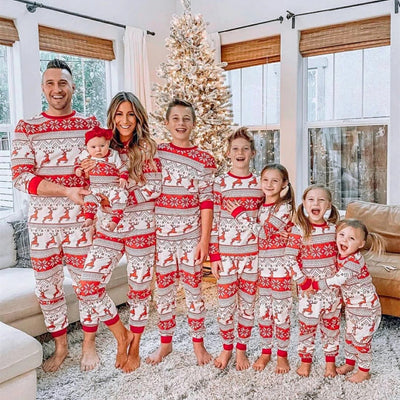 Family of eight wearing matching red and white Christmas pajamas with reindeer and snowflake patterns in a living room.