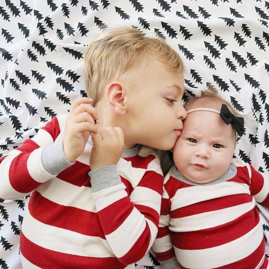 Family of four in matching red and white striped Christmas pajamas, sitting on a white rug with holiday decor. - Image 12