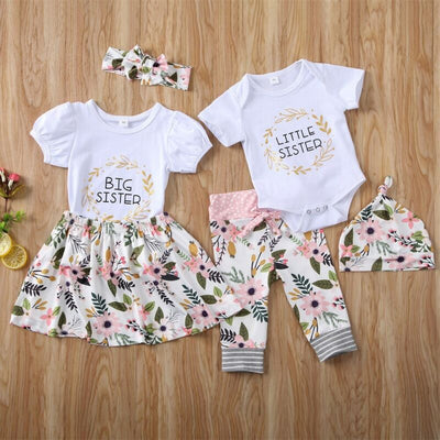 White 'Big Sister' top with floral skirt and 'Little Sister' bodysuit with floral pants and hat, matching sibling outfits.