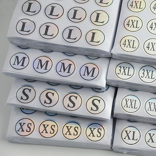 Stack of round clothing size stickers with laser color-changing background and black text, from XS to 4XL.