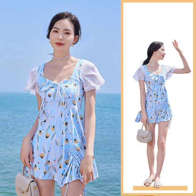 Woman in a light blue floral print swimsuit with sheer white short sleeves and a skirted bottom at the beach. - Image 4