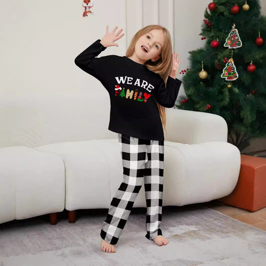 Family of four wearing matching black long-sleeve pajamas with "WE ARE FAMILY" text and black and white plaid bottoms. - Image 3