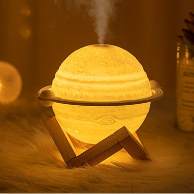 Yellow planet-shaped humidifier with a wooden stand emitting mist, next to a dark blue celestial gift bag. - Image 9