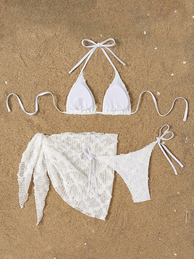 White lace halter bikini set with a matching mesh sarong, laid out on sand with sunglasses and a palm leaf. - Image 15