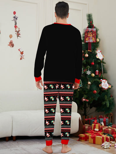 Man wearing black Christmas pajamas with a cartoon dinosaur, Santa Claus, and "Merry Christmas" text, standing by a decorated tree. - Image 17
