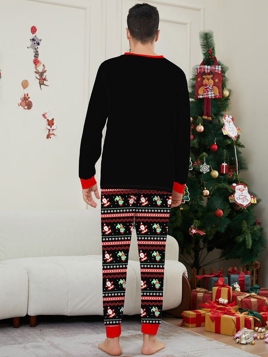 Man wearing black Christmas pajamas with a cartoon dinosaur, Santa Claus, and "Merry Christmas" text, standing by a decorated tree. - Image 17