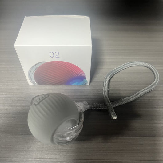 Gray intelligent automatic cat teasing ball with a clear section and braided cord, next to its white product box. - Image 13
