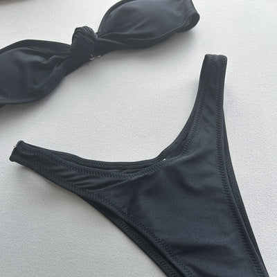 Woman wearing a black bandeau bikini top with a front knot and matching high-cut bottoms, accessorized with gold jewelry. - Image 25