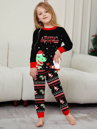 Man wearing black Christmas pajamas with a cartoon dinosaur, Santa Claus, and "Merry Christmas" text, standing by a decorated tree. - Image 35