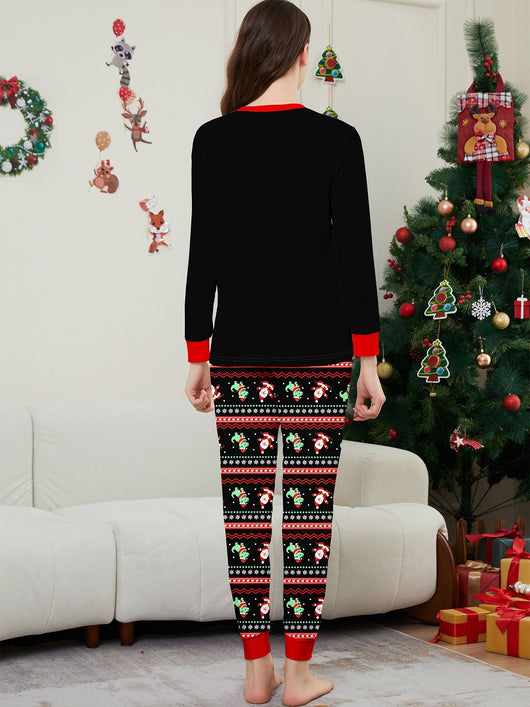 Man wearing black Christmas pajamas with a cartoon dinosaur, Santa Claus, and "Merry Christmas" text, standing by a decorated tree. - Image 19