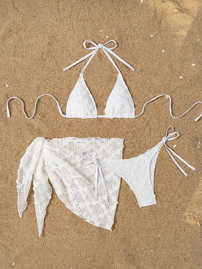 White lace halter bikini set with a matching mesh sarong, laid out on sand with sunglasses and a palm leaf. - Image 9