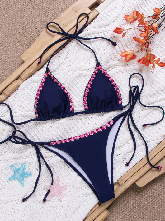 Navy blue bikini swimsuit set with pink floral lace trim on triangle top and tie-side bottoms, on a white knit blanket. - Image 6