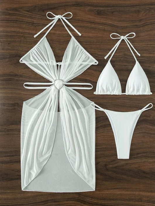 White three-piece halter neck bikini and sheer cover-up set with a heart-shaped embellishment, laid flat on wood. - Image 12