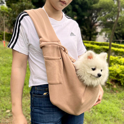 Person in white hoodie carrying a happy white dog in a navy blue pet sling bag outdoors. - Image 25