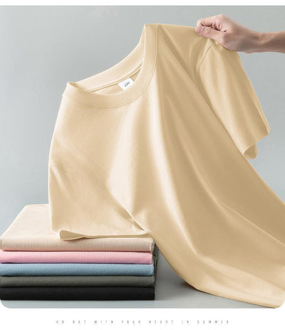 Light gray short-sleeve t-shirt with a round neck, held up to show its smooth fabric. A stack of folded t-shirts in various colors is visible in the background. - Image 20