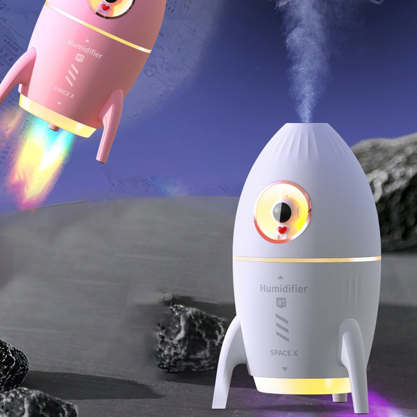 Pink rocket-shaped humidifier with an astronaut figurine in a circular window and a glowing yellow light band.