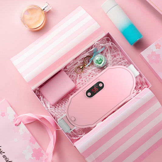 Pink stomach warming belt with vibration and heating, USB charging cable, two wormwood bags, and manual in a floral gift box.