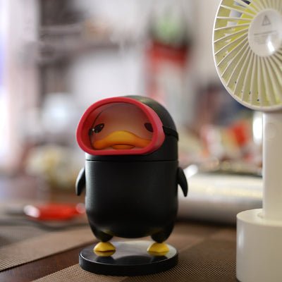Black diving duck spray humidifier with red goggles and yellow feet, standing on a dark base on a table. - Image 2