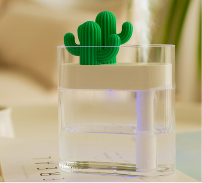 Transparent portable humidifier with a green cactus design on top, emitting mist on a wooden desk next to a laptop. - Image 16