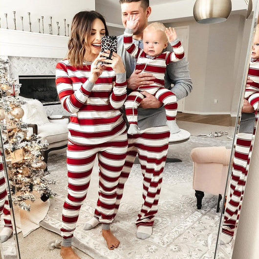 Family of three in matching red and white striped Christmas pajamas, posing for a mirror selfie in a festive living room.
