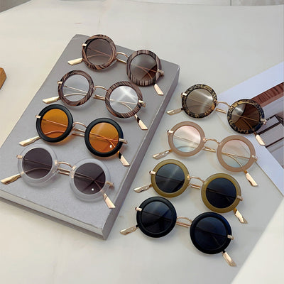 Small frame oval fashion sunglasses with black frames and vibrant orange lenses, held by a hand.
