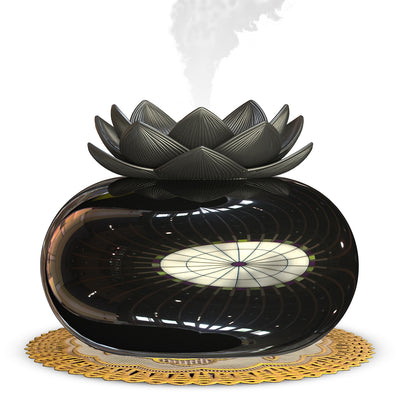 Black spherical aromatherapy humidifier with a lotus flower top, emitting mist, sitting on a gold decorative doily.