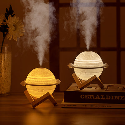 Yellow planet-shaped humidifier with a wooden stand emitting mist, next to a dark blue celestial gift bag. - Image 3