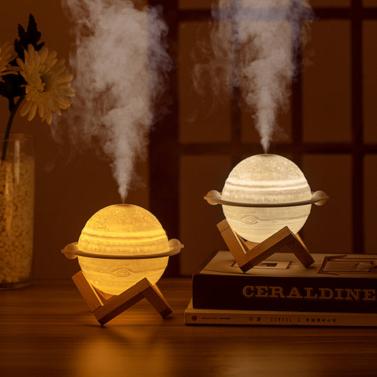 Yellow planet-shaped humidifier with a wooden stand emitting mist, next to a dark blue celestial gift bag. - Image 3