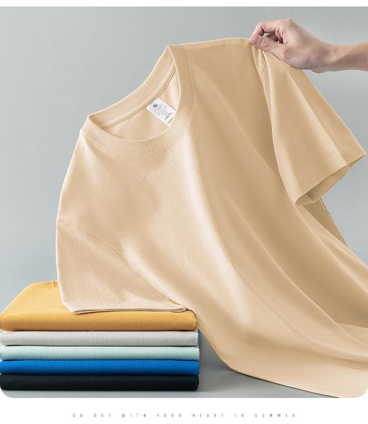Light gray short-sleeve t-shirt with a round neck, held up to show its smooth fabric. A stack of folded t-shirts in various colors is visible in the background. - Image 18