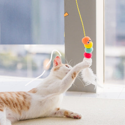 Colorful cat toy with pom-poms, googly eyes, white feathers, and a yellow elastic rope with a suction cup.