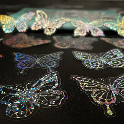 Transparent holographic butterfly laser stickers in various designs, including floral and moon elements, shown individually and in a 100-sheet pack. - Image 17