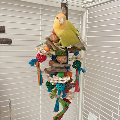 Hanging parrot toy made from natural wood, corn husk, and nuts with colorful strings and beads. A small yellow bird perches on the toy. - Image 11