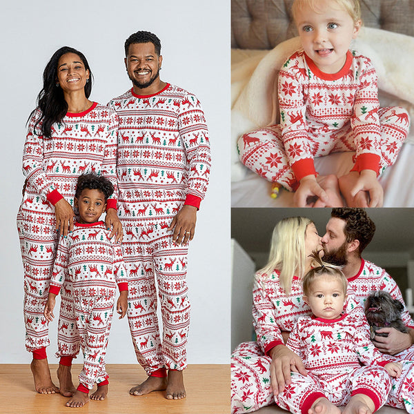 Family wearing matching white and red Christmas pajamas with elk and snowflake patterns, including a baby and a dog.