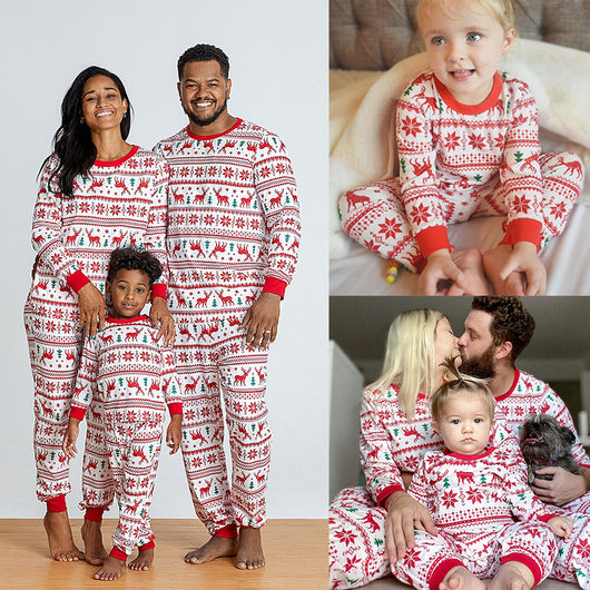 Family wearing matching white and red Christmas pajamas with elk and snowflake patterns, including a baby and a dog.