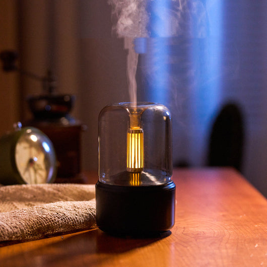 White cylindrical aroma diffuser with a clear top and an amber candlelight-effect LED light. - Image 3