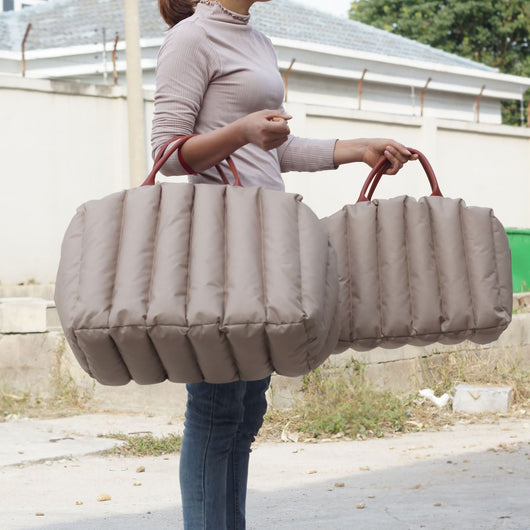 Light khaki quilted portable pet carrier with brown handles and a cream shoulder strap for car travel.