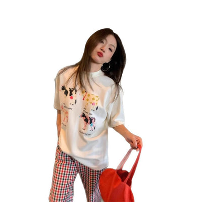 White loose-fit short-sleeve top with colorful retro cartoon cow print, modeled by a woman with plaid pants. - Image 5