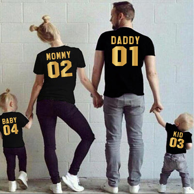 Child's black short-sleeved t-shirt with 'BABY 04' in gold print on the back, worn by a toddler in grass. - Image 13