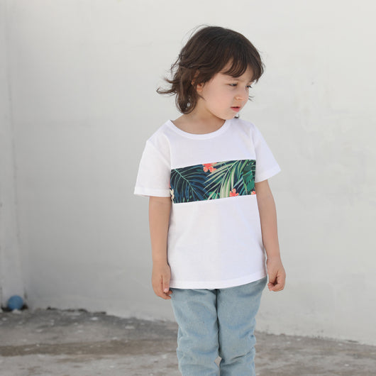 Child's white short-sleeve t-shirt with a horizontal tropical leaf and orange flower print band across the chest. - Image 7