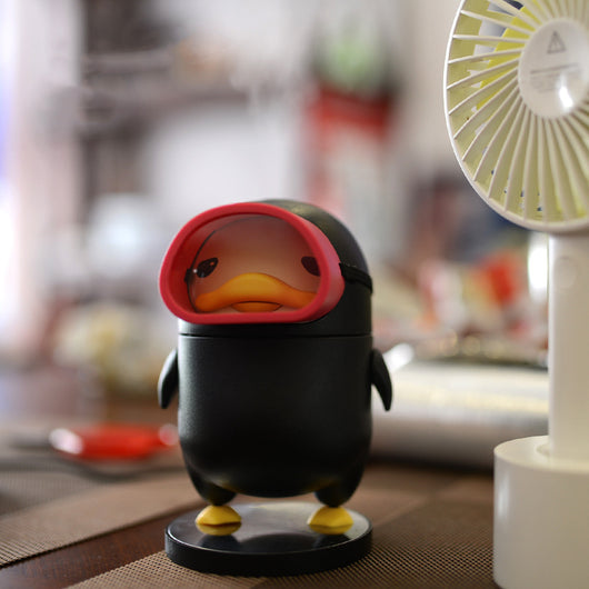 Black diving duck spray humidifier with red goggles and yellow feet, standing on a dark base on a table. - Image 7