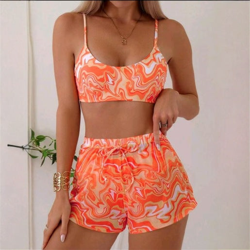 Red, orange, and white abstract swirl print three-piece bikini set with matching shorts, shown with a straw hat and sunglasses.