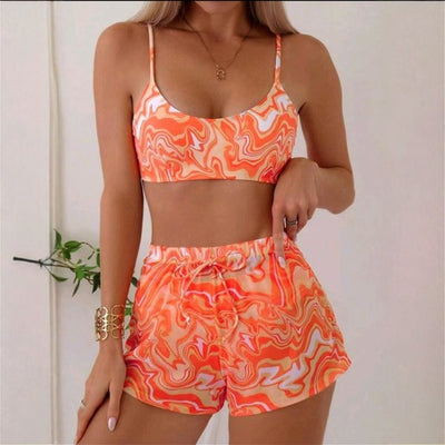Red, orange, and white abstract swirl print three-piece bikini set with matching shorts, shown with a straw hat and sunglasses.
