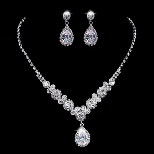 Sparkling silver-toned necklace and matching teardrop earrings set with clear stones, displayed on a black stand. - Image 8