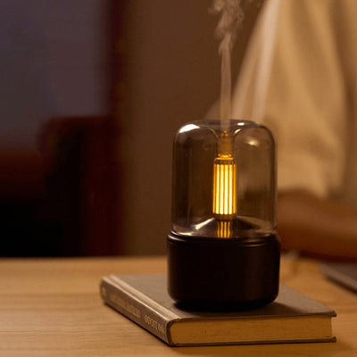 White cylindrical aroma diffuser with a clear top and an amber candlelight-effect LED light. - Image 4